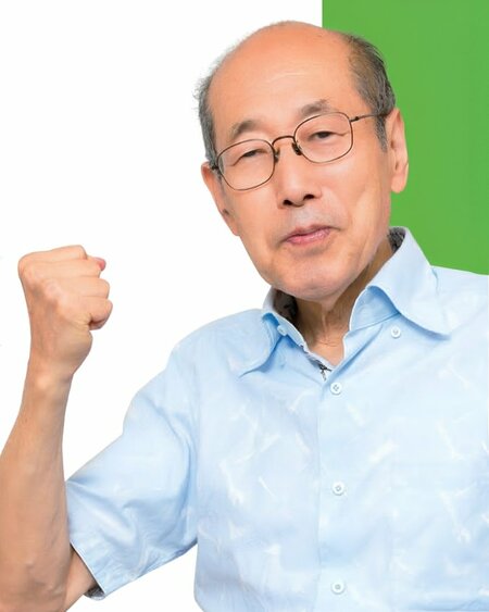 うす水色のシャツを着た桐谷さんが、片手を握ってこぶしを上げている写真。背景は白と緑。